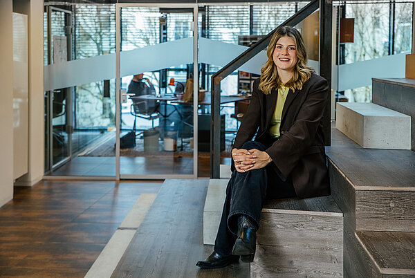 Lächelnde junge Frau sitzt auf einer Treppe in einem modernen Büro.