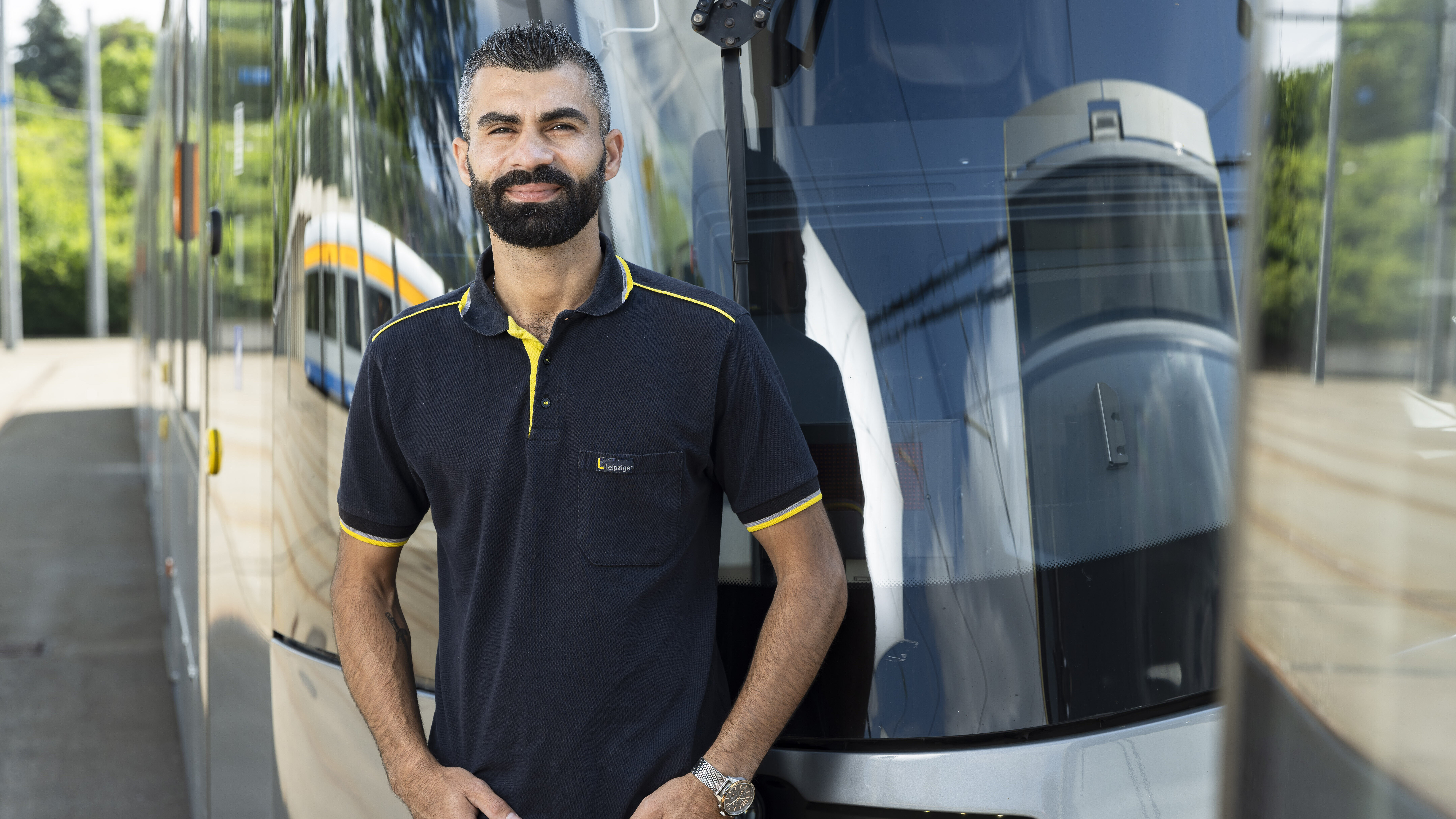 Nazar Arab steht vor einer Straßenbahn. Er hat schwarze, kurze Haare, hat die Hände in den Taschen und trägt ein dunkelblaues T-Shirt der Leipziger Gruppe.