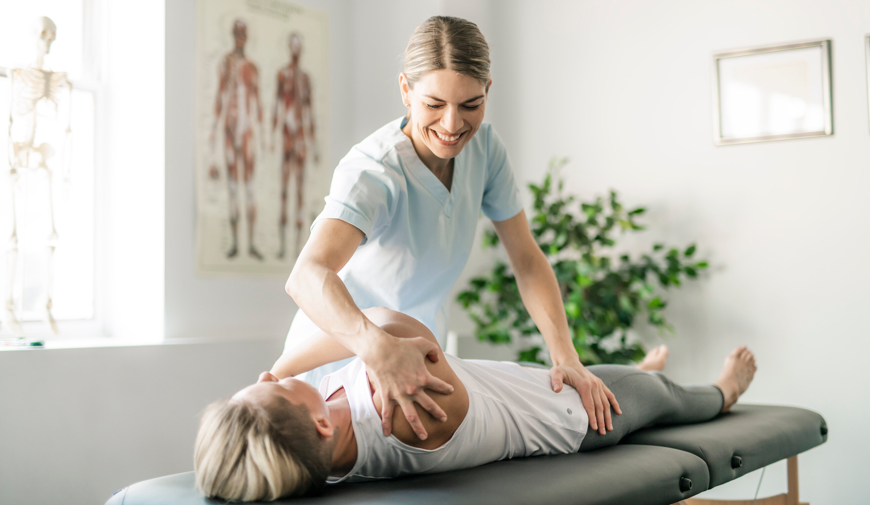 Foto: Ein Mann auf einer Massageliege wir von einer Physiotherapeutin gedehnt.