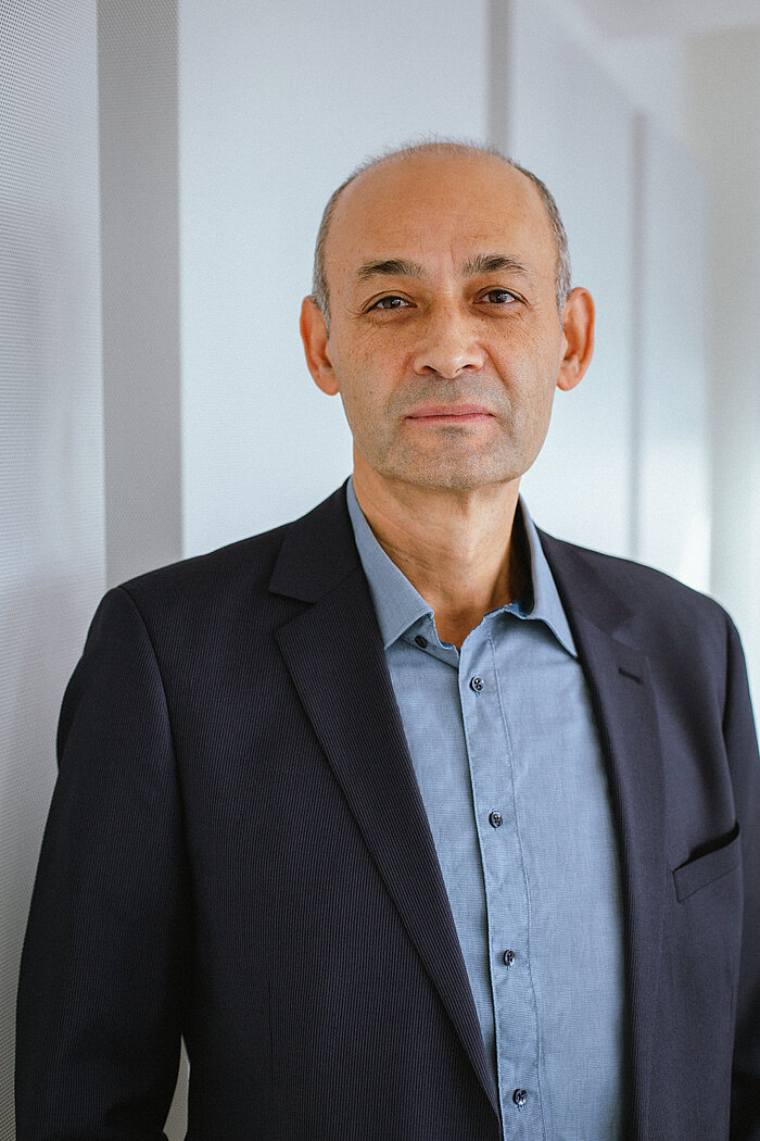 Foto: Porträt von Süleyman Kacmaz. Er schaut in die Kamera, trägt ein hellblaues Hemd und ein dunkelblaues Sakko.