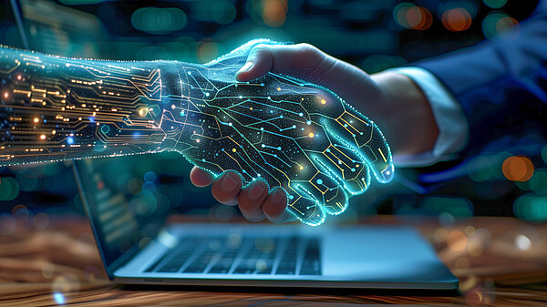 Eine symbolische Darstellung von Technologie und menschlicher Zusammenarbeit. Eine Hand, die eine menschliche Hand schüttelt, ist futuristisch und transparent dargestellt, mit leuchtenden Leiterbahnen und digitalen Schaltkreisen, die eine Art künstliche Intelligenz oder digitale Verbindung symbolisieren. Die andere Hand ist eine normale, menschliche Hand, die einen Anzugärmel trägt. Der Handschlag findet über einem geöffneten Laptop statt. Der Hintergrund ist unscharf und dunkel, mit Lichtern, die eine städtische oder technologische Umgebung andeuten.