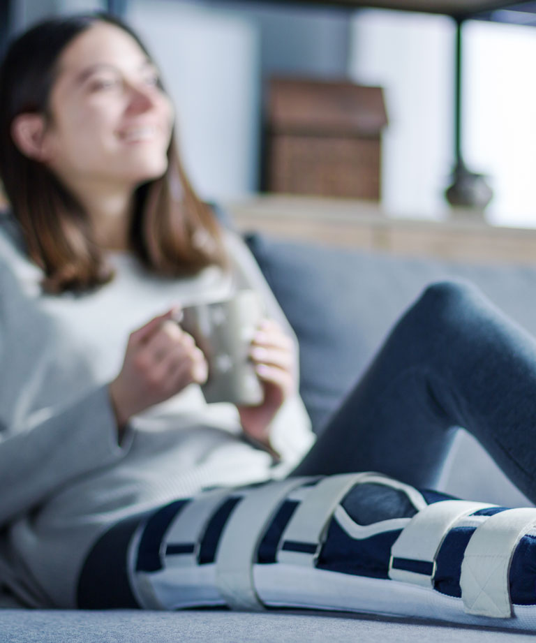 Frau mit vergipsten Bein sitzt auf Couch
