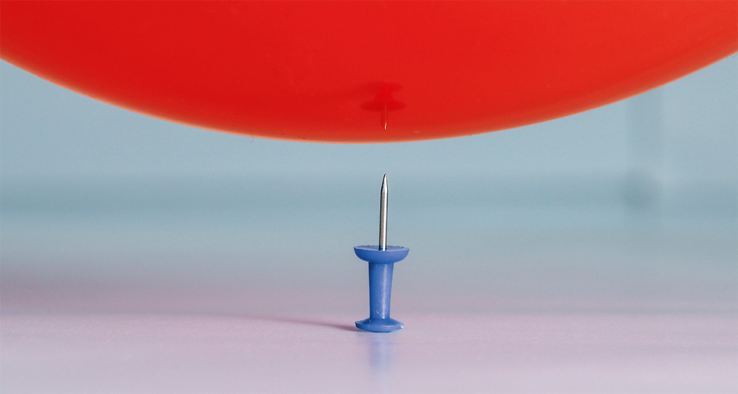Eine Nadel droht einen Luftballon zum Platzen zu bringen
