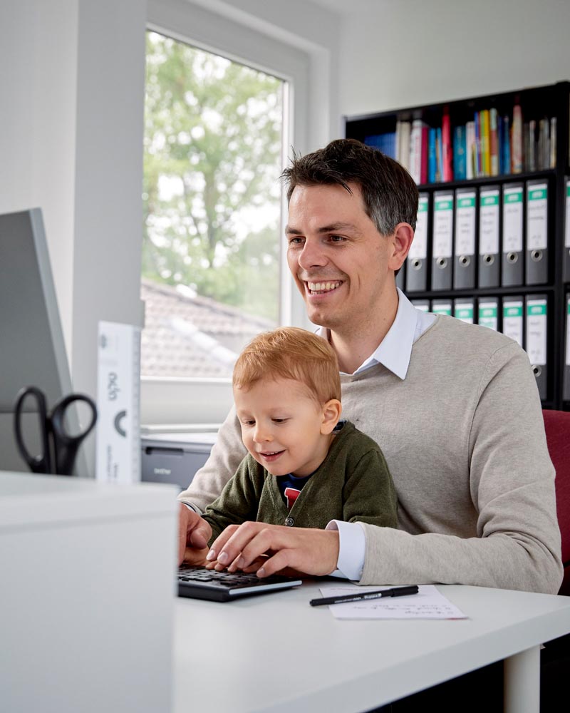 Diedrich Bremer arbeitet am Laptop, auf seinem Schoß sitzt sein Sohn